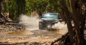 A black Toyota Land Cruiser driving through a stream in a wooded area
