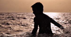 Young boy playing in the ocean near sunset