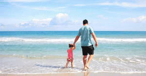 Young father and daughter walking on the beach holding hands