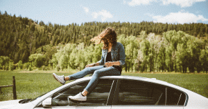 Woman sitting on the roof of her car, with the wind blowing her hair into her face